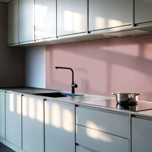 May include: A modern kitchen with gray cabinets and a pink backsplash. A black faucet is mounted above a stainless steel sink. A pot sits on a black electric stovetop.