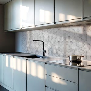 Puede incluir: Una cocina moderna con gabinetes grises y una estufa de acero inoxidable. El salpicadero está hecho de azulejos hexagonales grises. Un grifo negro está montado sobre un fregadero de acero inoxidable.