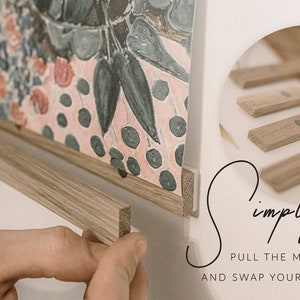 May include: A close-up of a wooden frame with magnets holding a colorful print. The text "Simply pull the magnets apart and swap your prints over" is visible below the frame.