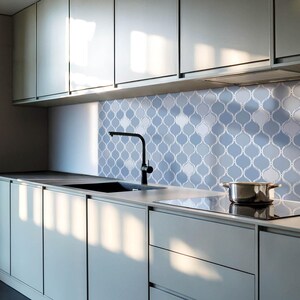 Puede incluir: Cocina moderna con armarios gris claro, un fregadero negro y un salpicadero con estampado azul y blanco. Una olla de acero inoxidable está sobre una placa de cocina negra. El grifo es negro.