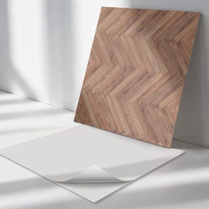 Puede incluir: Una muestra de papel tapiz blanco autoadhesivo con un patrón de veta de madera. La muestra está sobre una superficie blanca con sombras.