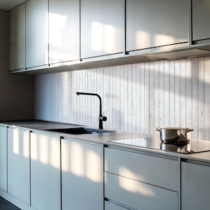 Puede incluir: Una cocina moderna con armarios grises y un salpicadero de madera blanca. Un grifo negro está montado sobre un fregadero de acero inoxidable. Una placa de cocción eléctrica negra es visible en primer plano.