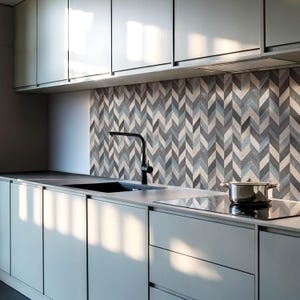 Puede incluir: Una cocina moderna con armarios grises y un grifo negro. El salpicadero es un patrón de espiga de azulejos grises, azules y beige.