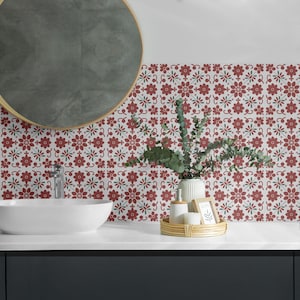 May include: A bathroom vanity with a white sink and a round mirror. The backsplash is tiled with red and green floral patterned tiles. A small plant in a white vase and a tray with toiletries are on the counter.