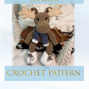 Könnte beinhalten: Häkelanleitung für einen braunen Elch namens "Muffin the Moose", der blaue und weiße Schlittschuhe trägt. Der Elch sitzt auf einem Holzschlitten mit weißem Schnee und kleinen weißen Bäumen im Hintergrund.