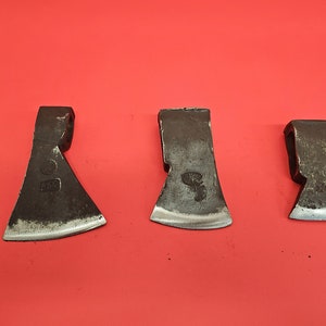 May include: Three small, black metal hand axes with slightly curved blades. The axes have a worn, rustic look.