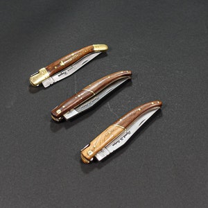 May include: Three pocket knives with wooden handles and brass accents. The blades are closed and the handles are decorated with intricate patterns.
