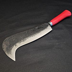 May include: A curved, black-handled, forged steel knife with a red plastic handle. The blade is curved and has a rough, hammered finish.