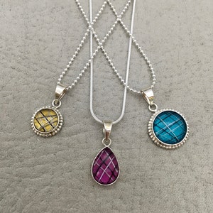 May include: Three silver necklaces with different pendants. The pendants are round with a patterned design in gold, teal, and pink.