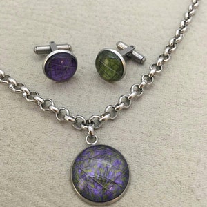 May include: A silver-toned necklace with a matching pendant and a pair of cufflinks. The pendant and cufflinks feature a circular design with a purple and green pattern. The chain and cufflink hardware are a shiny silver color.
