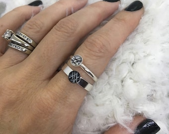 May include: Two silver rings with black and white patterned inlays. The rings are stacked on a finger.