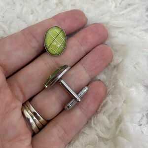 May include: A pair of cufflinks with a lime green oval design and a silver grid pattern. The cufflinks have a silver metal backing and a post for securing them to a shirt cuff. The design is repeated on the oval button.