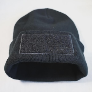 Puede incluir: Gorro negro con un parche de velcro negro en la parte delantera. El parche tiene la palabra "LIFE" bordada.