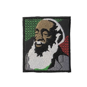 May include: Embroidered patch featuring a portrait of a man with a white beard and closed eyes. The patch has a black border with green and red accents. The man is wearing a gray suit jacket.