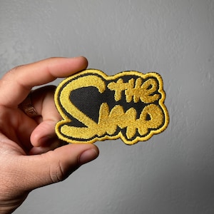 May include: A black and gold embroidered patch with the text "The Who" in a stylized font.