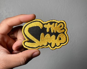 May include: A black and gold embroidered patch with the text "The Who" in a stylized font.