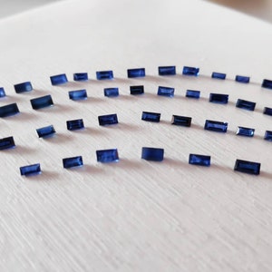 Puede incluir: Una colección de pequeñas piedras preciosas azules rectangulares dispuestas en forma de semicírculo sobre una superficie blanca.