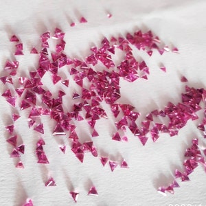 Puede incluir: Una dispersión de pequeñas piedras preciosas rosadas triangulares sobre una superficie blanca.