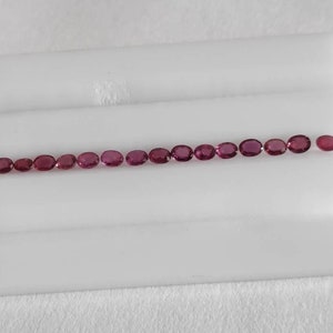 Può includere: Una fila di gemme ovali, di un rosa intenso, disposte su una superficie bianca a gradini. Le gemme presentano una variazione di intensità cromatica, dal rosa chiaro al rosa scuro. Probabilmente rubini o zaffiri rosa.