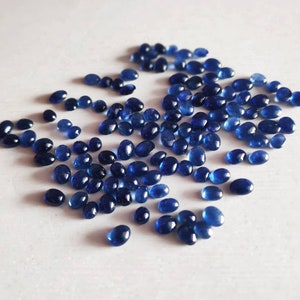 May include: A scattering of oval-shaped, dark blue gemstones on a white surface.