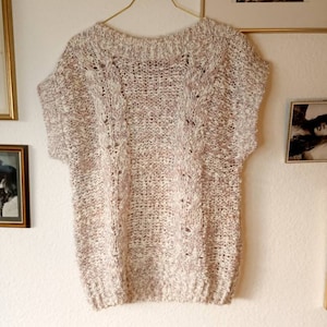 May include: A white and pink knitted sweater with short sleeves and a cable knit pattern.