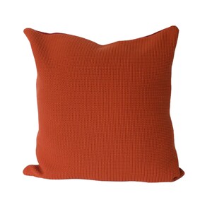 May include: A solid orange throw pillow with a textured woven fabric. The pillow is square shaped and has a simple design.