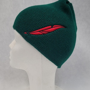 May include: A dark green knitted beanie with a red embroidered feather design.
