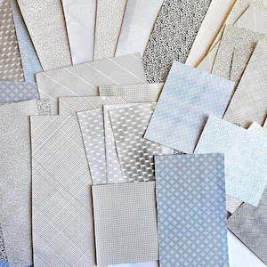 May include: A collection of patterned paper sheets in various shades of gray and blue. The sheets feature diverse designs, including stripes, dots, and geometric patterns. The papers are arranged in a fan-like display, showcasing the variety of textures and styles.