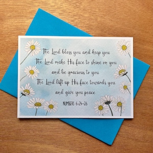 May include: A white card with a blue watercolour background and white daisies. The card features a bible verse from Numbers 6:24-26, "The Lord bless you and keep you. The Lord make His face to shine on you and be gracious to you. The Lord lift up His face towards you and give you peace."