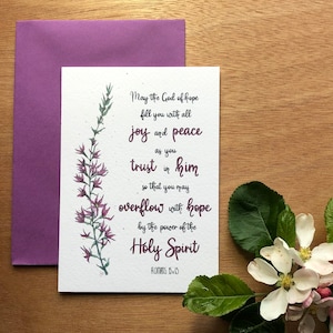 May include: A card featuring a purple flower illustration and a quote from Romans 15:13. The quote reads: "May the God of hope fill you with all joy and peace as you trust in him so that you may overflow with hope by the power of the Holy Spirit."