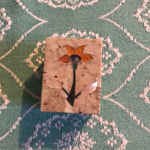 May include: A small, square, white marble box with a floral design inlaid with colourful stones. The flower is orange, green, and blue, with white leaves.