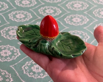 May include: A ceramic trinket dish shaped like a green leaf with a red and yellow acorn on top.
