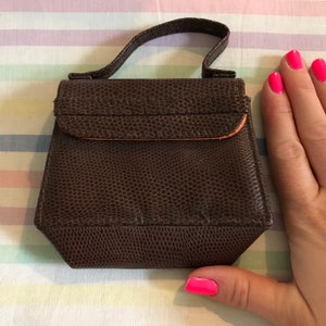 May include: A small brown leather handbag with a top handle. The bag has a textured, pebbled surface and a flap closure with a brown leather strap.