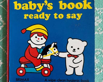 May include: A blue baby's book with the title "baby's book ready to say" in yellow letters. The book features illustrations of a child on a rocking horse and a teddy bear. The book is labelled "A wipe-clean hygienic book" and "BRIMAX 0501".