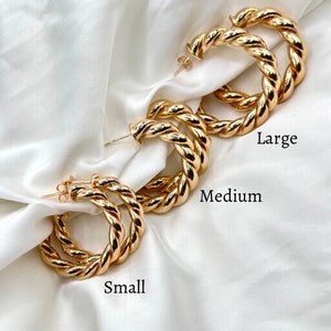 May include: Three pairs of gold-toned hoop earrings in different sizes: small, medium, and large. The earrings are made of twisted metal and have a polished finish.