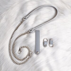 May include: A silver chain strap with a gray leather strap and two gray leather strap connectors. The strap is designed for a handbag or purse.