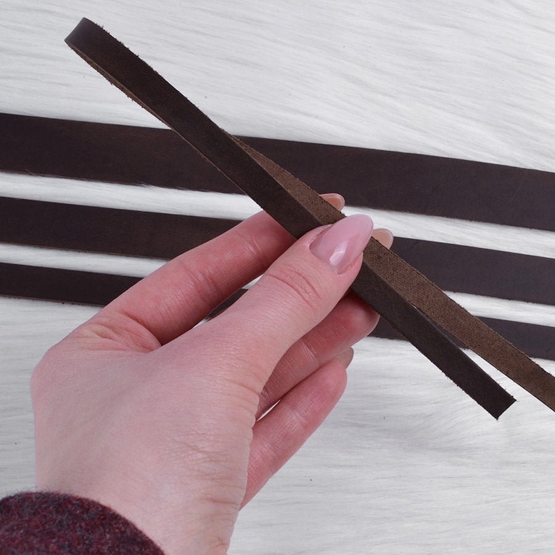 May include: A close-up of a brown leather strap, held in a hand. The strap is smooth and supple, with a slightly textured surface.