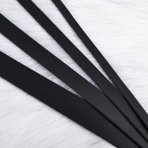 May include: Five black leather straps of varying lengths arranged in a fan shape on a white fuzzy surface.