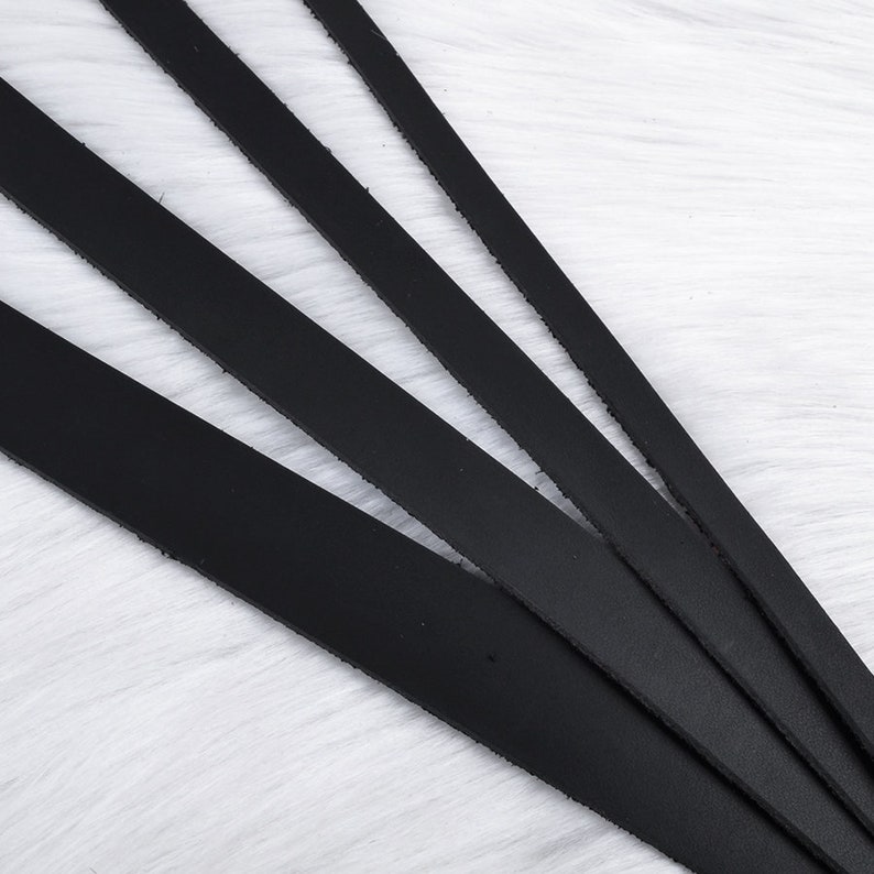 May include: Five black leather straps of varying lengths arranged in a fan shape on a white fuzzy surface.