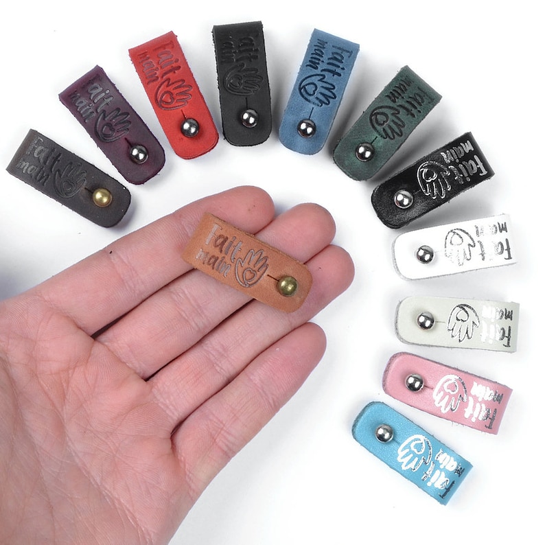 May include: Assortment of ten leather cable organizers in various colors, each with a silver metal bead and the text "Fait main" embossed on the leather.