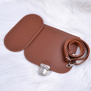 May include: Brown leather bag making kit with a metal clasp, a strap, and two pieces of leather with holes for stitching.