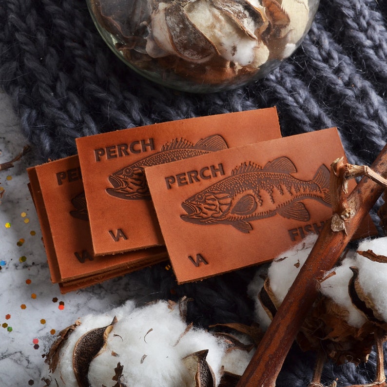 May include: Close-up of a stack of brown leather labels with an embossed image of a fish and the word "PERCH".