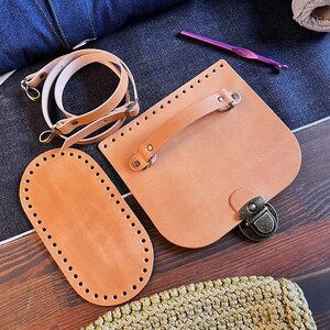 May include: A set of leather crafting supplies including a brown leather bag with a handle and a metal clasp, a brown leather oval shape with holes around the edge, and a brown leather strap with metal hardware.