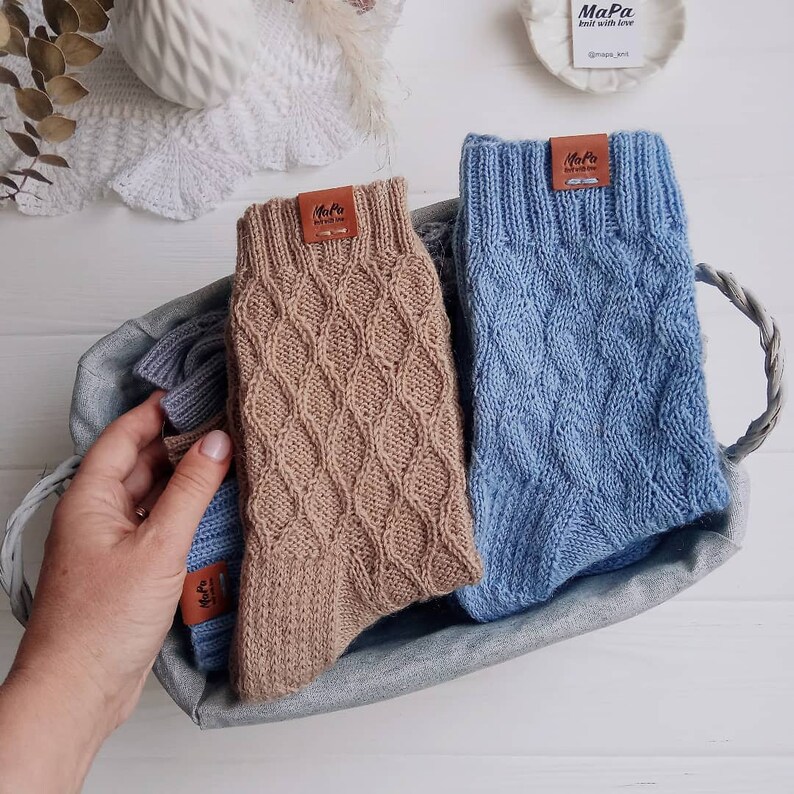 Puede incluir: Dos pares de calcetines de punto en una cesta tejida. Un par es marr&oacute;n y el otro es azul. Ambos pares tienen una etiqueta de cuero con el texto "MaPa knit with love @mapa_knit".
