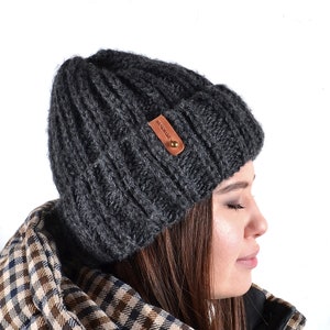 Op de afbeelding: Een donkergrijze gebreide beanie met een bruin lederen label waarop "BONDEDWARE" staat.
