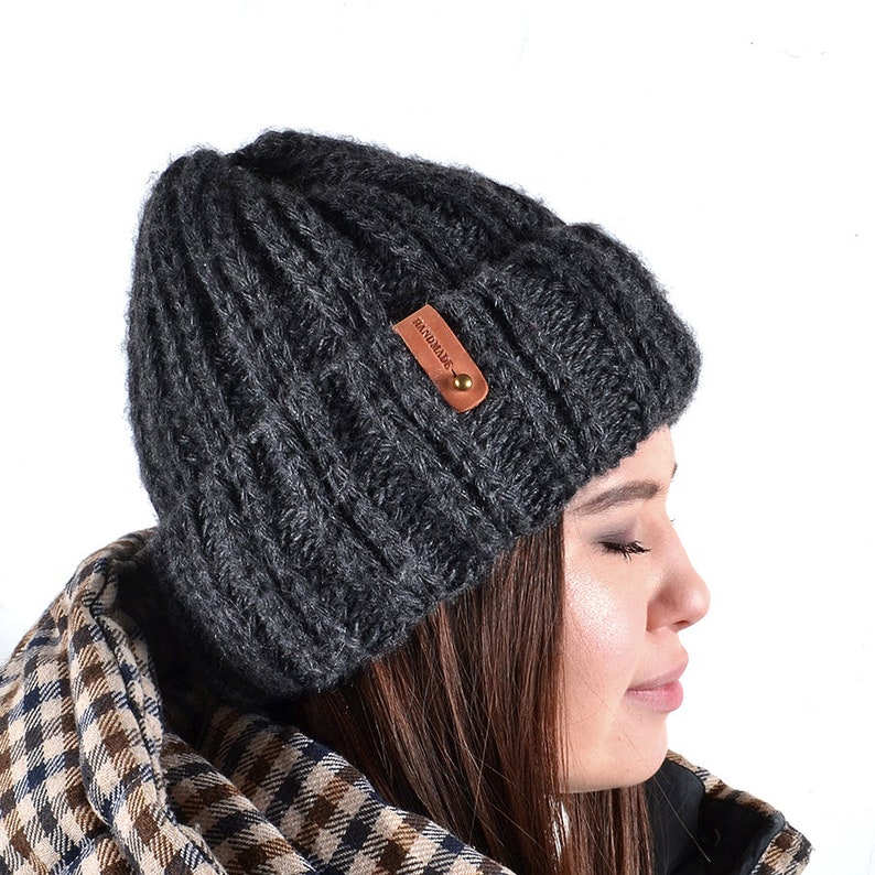 Op de afbeelding: Een donkergrijze gebreide beanie met een bruin lederen label waarop "BONDEDWARE" staat.