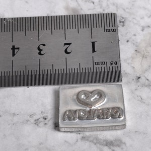 May include: A silver metal stamp with a heart and the word "AVOLATA" engraved on it. The stamp is about 1 inch wide and 1 inch tall.