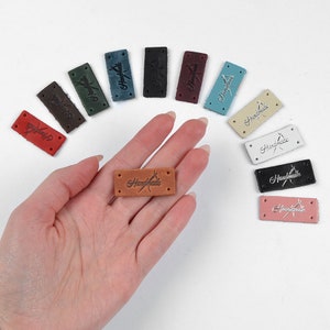 May include: Assortment of 12 leather labels with the word "Handmade" embossed in different colors, including brown, black, white, pink, and blue.