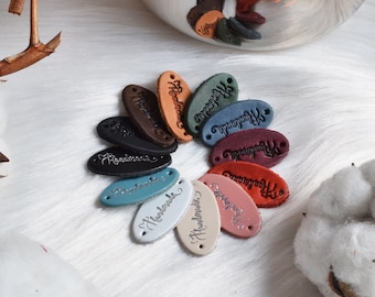Könnte beinhalten: Eine Sammlung ovaler Lederanhänger in verschiedenen Farben, jeder mit dem Wort "Handmade" in einer Schriftart geprägt.