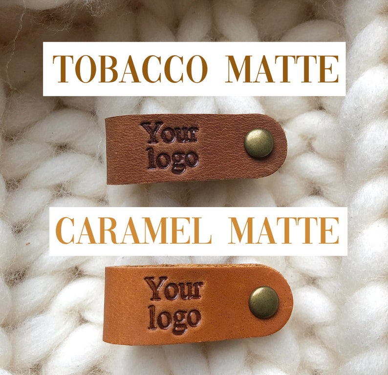 Puede incluir: Dos etiquetas de cuero con el texto "Your logo" en relieve. La etiqueta superior es de color tabaco mate y la etiqueta inferior es de color caramelo mate.